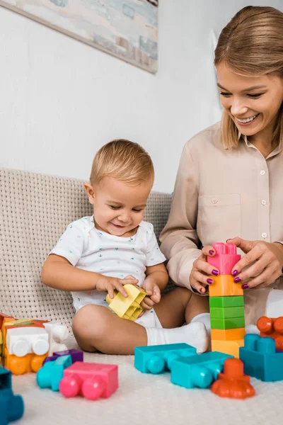Adorable toddler sitting on sofa and playing with colorful cubes and mother — Stock Photo