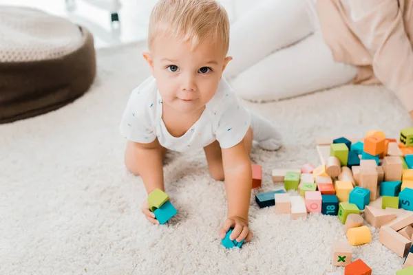 Adorable niño jugando con cubos de colores y mirando a la cámara - foto de stock