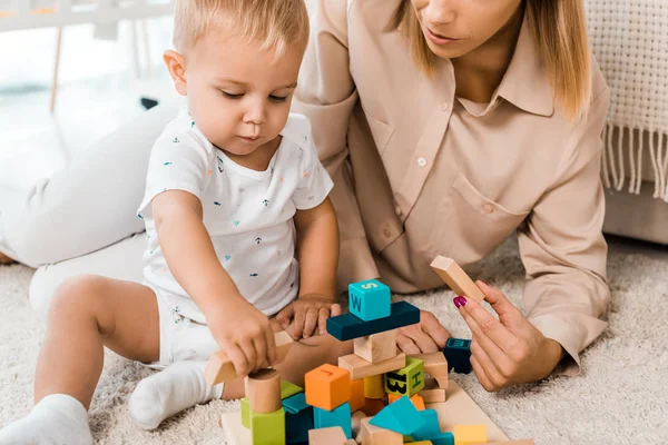 Vista recortada de adorable niño jugando con cubos de colores y la madre en la habitación de la guardería - foto de stock