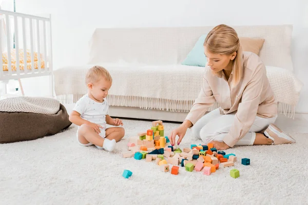 Entzückendes Kleinkind spielt mit bunten Würfeln und Mutter im Kinderzimmer — Stockfoto