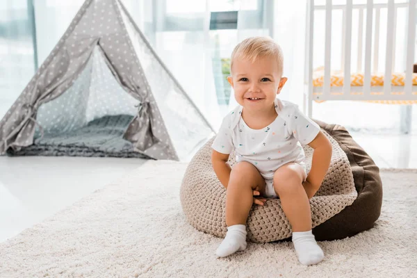 Entzückend lächelndes Kleinkind sitzt auf Bohnensackstuhl und blickt in Kinderzimmer in die Kamera — Stockfoto