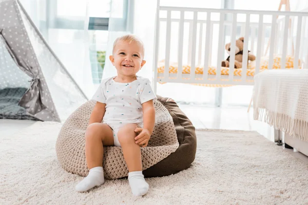 Adorable sonriente niño sentado en la silla de la bolsa de frijol en la habitación del vivero - foto de stock