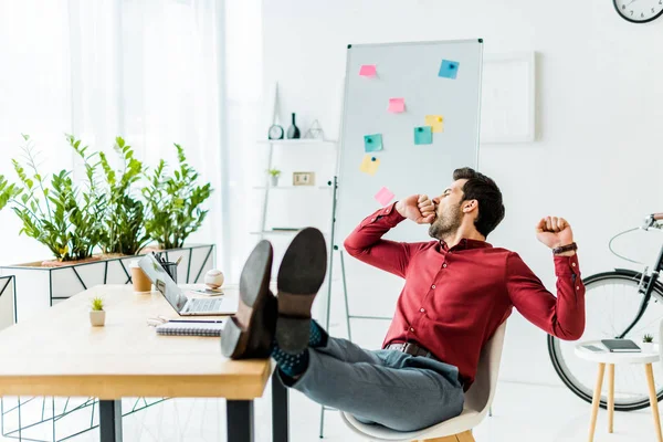 Tired businessman with legs on table yawning in office — Stock Photo