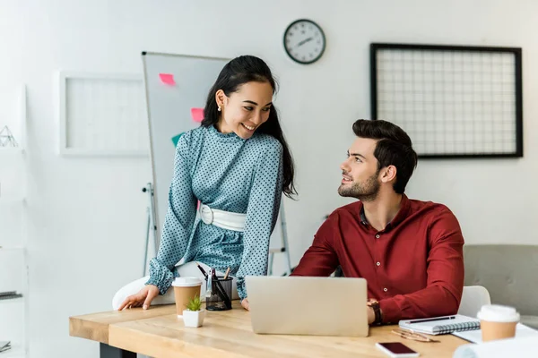 Lächelnde multiethnische Kollegen mit Laptop im Büro — Stockfoto