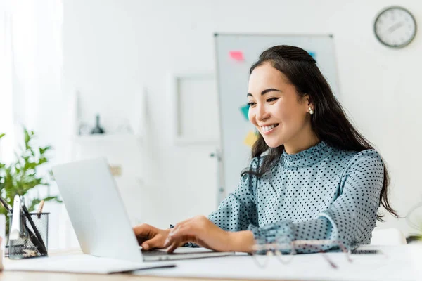 Schöne lächelnde asiatische Geschäftsfrau sitzt am Schreibtisch und benutzt Laptop im Büro — Stockfoto