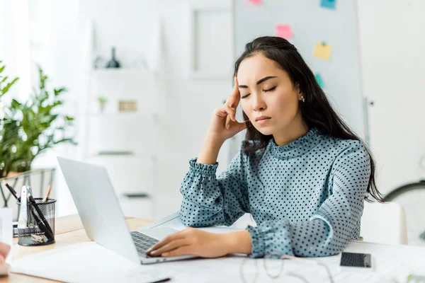 Stressed asian businesswoman sitting at computer desk and having headache in office — Stock Photo