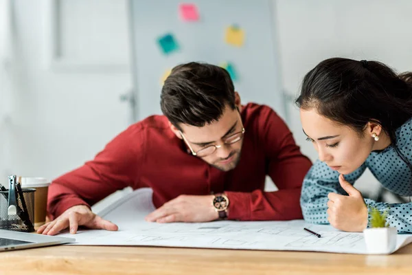 Focused multicultural couple of architects working on blueprint in office — Stock Photo