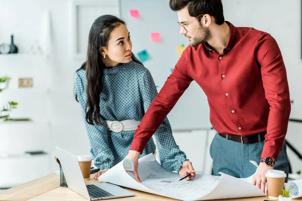 Focused multicultural couple of architects working on blueprint in office — Stock Photo