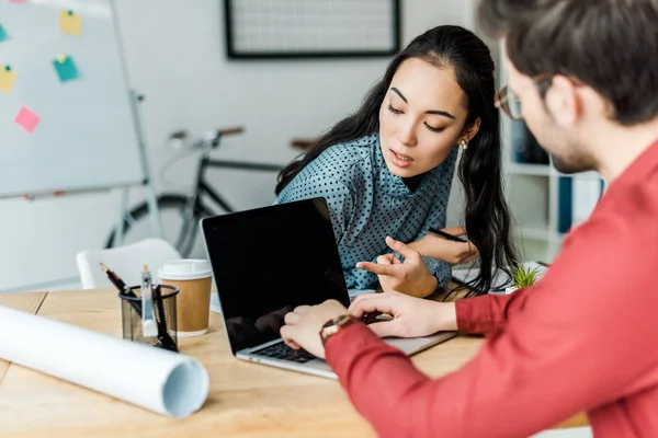 Pareja de arquitectos usando portátil con pantalla en blanco en la oficina - foto de stock