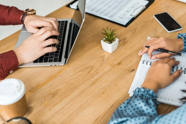 Partial view of colleagues sitting at table and using laptop in office — Stock Photo