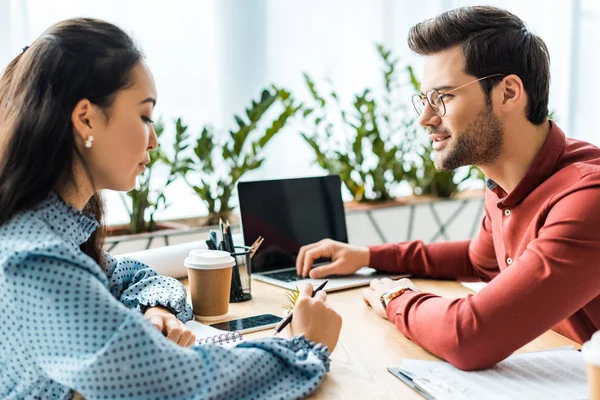 Colleghi multiculturali seduti a tavola e che utilizzano il computer portatile in carica — Foto stock