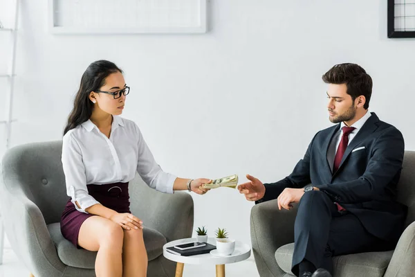 Asian businesswoman in formal wear giving money to businessman in office — Stock Photo