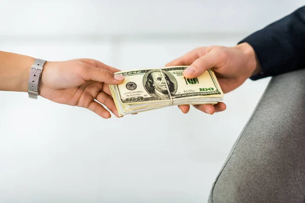 Cropped view of businesswoman giving dollar banknotes to businessman in office — Stock Photo