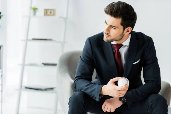 Homme d'affaires en tenue de cérémonie assis sur un fauteuil et tenant une balle de golf au bureau — Photo de stock