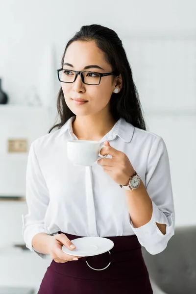 Attractive asian businesswoman in glasses and formal wear having coffee break in office — Stock Photo