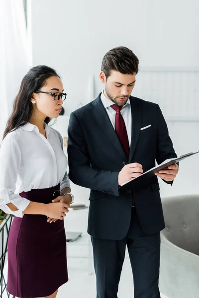 Des hommes d'affaires multiethniques concentrés dans l'habillement formel signant un contrat au bureau — Photo de stock