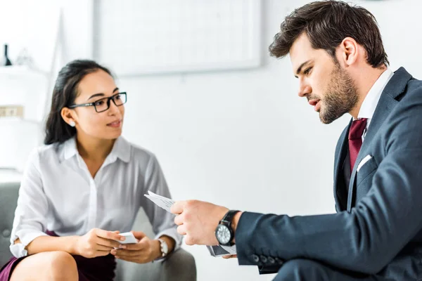 Asiático mujer de negocios mirando a hombre de negocios con periódico en oficina - foto de stock