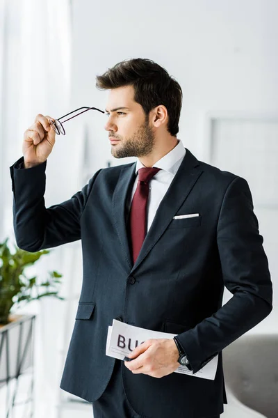 Bel homme d'affaires en tenue formelle tenant journal et portant des lunettes au bureau — Photo de stock