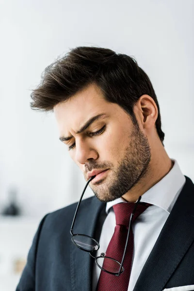 Serious handsome businessman in formal wear biting glasses in office — Stock Photo