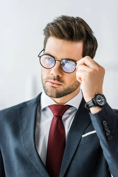 Guapo hombre de negocios en ropa formal ajustando gafas en la oficina - foto de stock