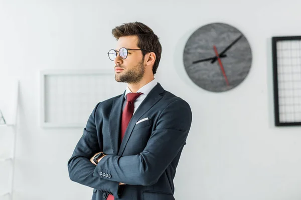 Handsome businessman in formal wear and glasses with arms crossed in office — Stock Photo