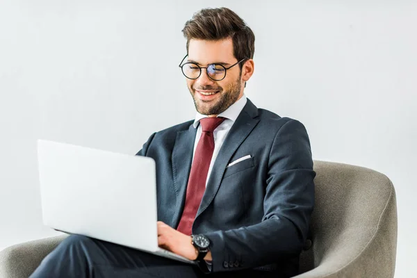 Lächelnder Geschäftsmann in offizieller Kleidung sitzt auf Sessel und benutzt Laptop im Büro — Stockfoto