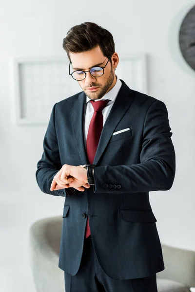 Schöner Geschäftsmann in formeller Kleidung, der im Büro auf die Uhr schaut — Stockfoto