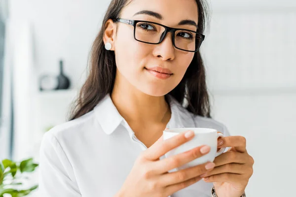 Attractive asian businesswoman in glasses having coffee break in office — Stock Photo