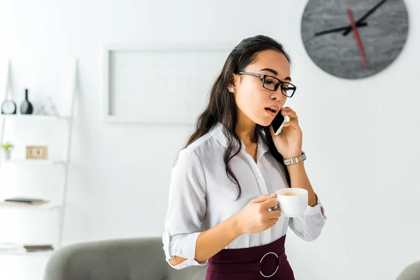 Beautiful asian businesswoman talking on smartphone while having coffee break in office — Stock Photo