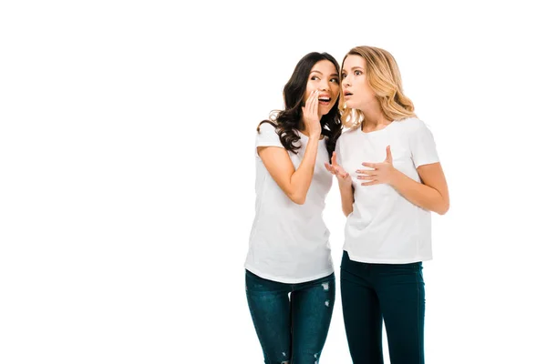 Smiling young woman whispering something to shocked girlfriend isolated on white — Stock Photo