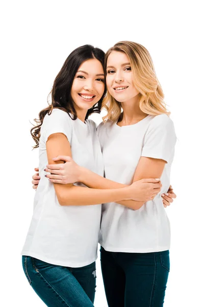 Mulheres jovens felizes em camisetas brancas abraçando e sorrindo para a câmera isolada no branco — Fotografia de Stock