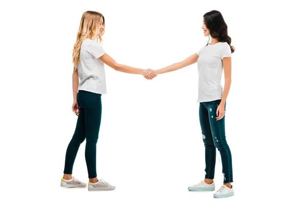 Visão lateral de mulheres jovens apertando as mãos isoladas no branco — Fotografia de Stock