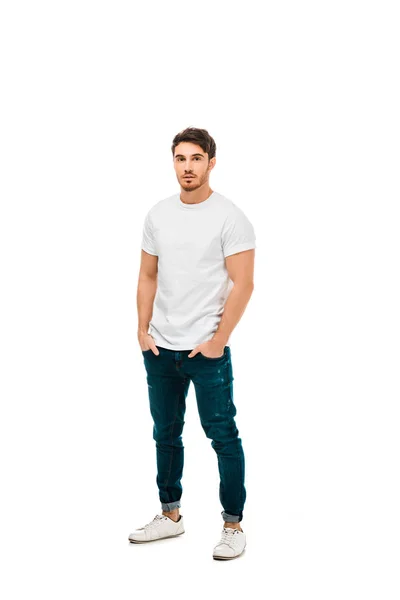 Full length view of handsome young man standing with hands in pockets and looking at camera isolated on white — Stock Photo