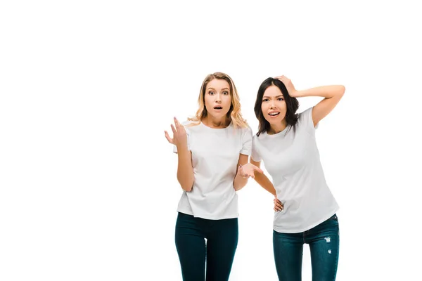 Scioccate giovani donne in t-shirt bianche guardando la fotocamera isolata su bianco — Foto stock