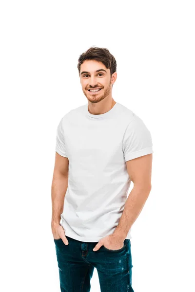 Красивий щасливий молодий чоловік стоїть з руками в кишенях і посміхається на камеру ізольовано на білому — стокове фото
