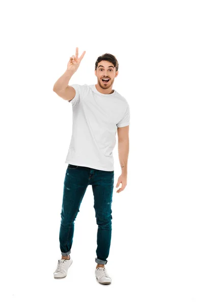 Ganzkörperansicht eines glücklichen jungen Mannes, der Siegeszeichen zeigt und isoliert auf Weiß in die Kamera lächelt — Stockfoto