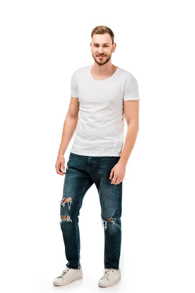 Vista completa de hombre joven guapo en camiseta blanca y jeans sonriendo a la cámara aislado en blanco - foto de stock