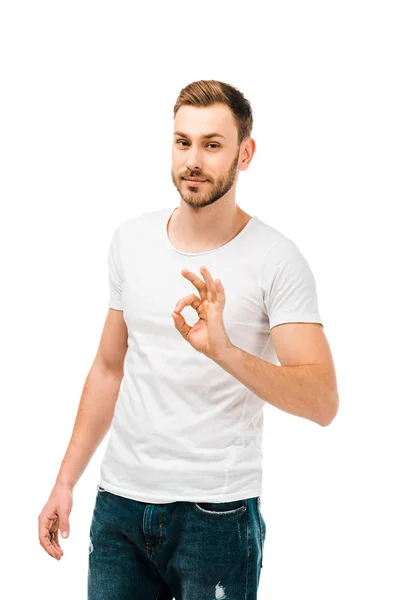 Schöner junger Mann in weißem T-Shirt zeigt ok Zeichen und schaut in die Kamera isoliert auf weiß — Stockfoto