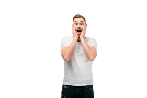 Shocked young man standing with hands on face and looking at camera isolated on white — Stock Photo