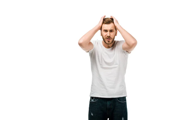 Jeune homme frustré en t-shirt blanc debout avec les mains sur la tête et regardant la caméra isolée sur blanc — Photo de stock