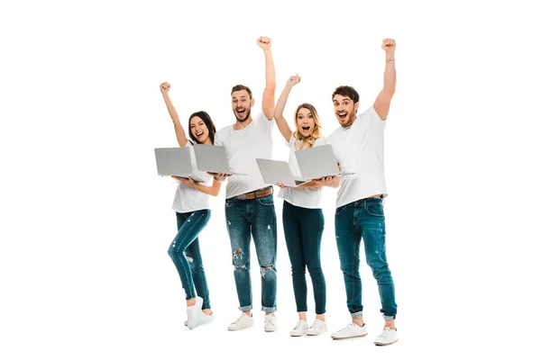 Jovens amigos animados com laptops levantando as mãos e sorrindo para a câmera isolada no branco — Fotografia de Stock