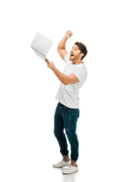 Excited young man holding laptop and shaking fist isolated on white — Stock Photo