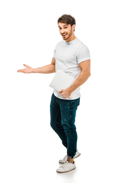 Full length view of handsome young man holding laptop and smiling at camera isolated on white — Stock Photo