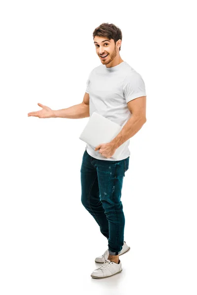 Vista de cuerpo entero del joven guapo sosteniendo el ordenador portátil y sonriendo a la cámara aislada en blanco - foto de stock