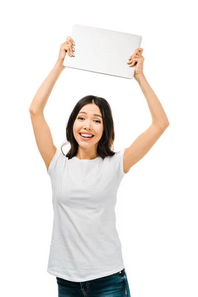 Glücklich junge Frau hält Laptop über Kopf und lächelt in Kamera isoliert auf weiß — Stockfoto