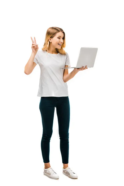 Щаслива молода жінка тримає ноутбук і показує знак перемоги ізольовано на білому — стокове фото