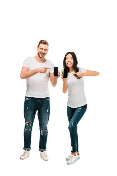 Heureux jeune couple pointant vers les smartphones avec des écrans vides isolés sur blanc — Photo de stock