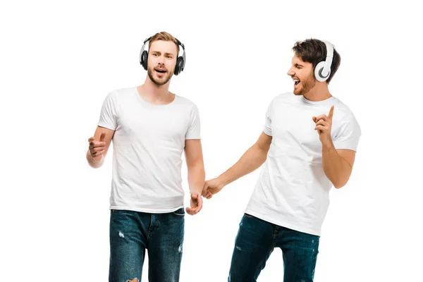 Jeunes hommes souriants écoutant de la musique dans des écouteurs et chantant isolés sur blanc — Photo de stock