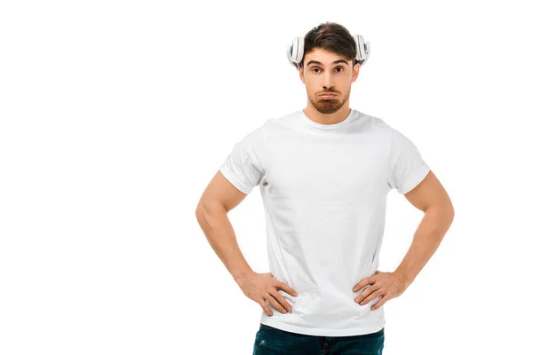 Hombre serio con auriculares en la cabeza de pie con las manos en la cintura y mirando a la cámara aislada en blanco - foto de stock