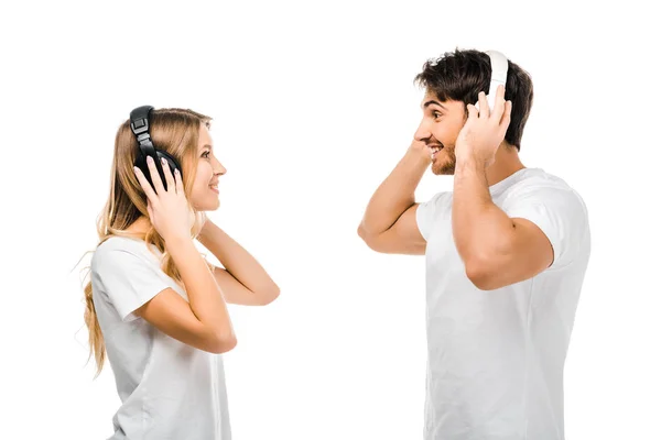 Vista lateral de pareja joven escuchando música en auriculares y sonriéndose aislados en blanco - foto de stock